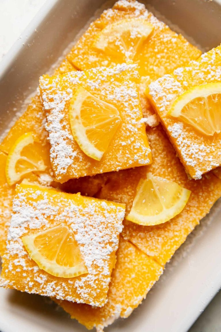 Overhead view of a pan of lemon bars topped with lemon wedges and powdered sugar. 