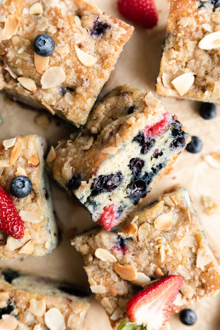 Close up view of pieces of mixed berry breakfast cake topped with slivered almonds and fresh berries. 